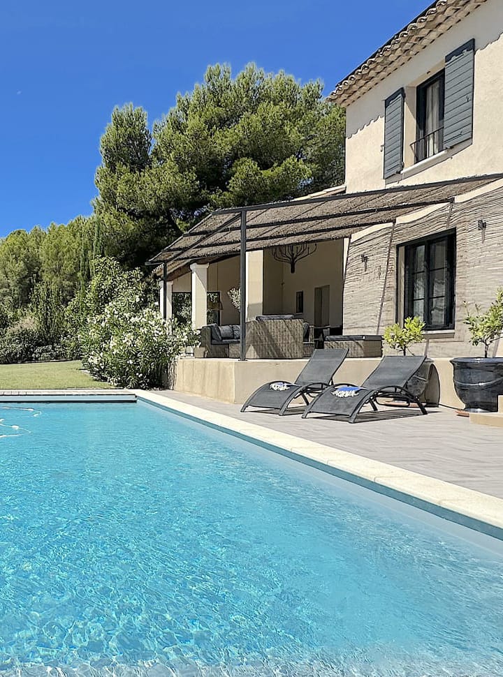 Vue rapprochée de la piscine d’une villa provençale, avec une terrasse ombragée, des transats modernes et un jardin luxuriant sous un ciel bleu limpide.