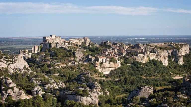 Vue panoramique des Baux-de-Provence, un village perché entouré de falaises rocheuses et de végétation luxuriante.